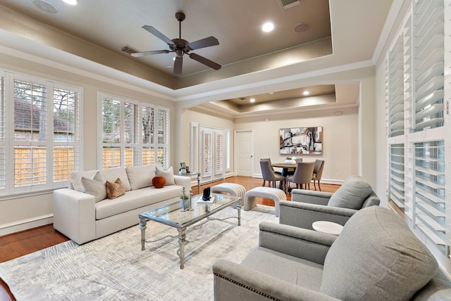 living area featuring a ceiling fan, wood finished floors, baseboards, ornamental molding, and a raised ceiling