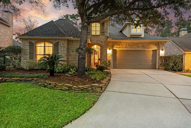 view of front of property featuring driveway, stone siding, a garage, and roof with shingles