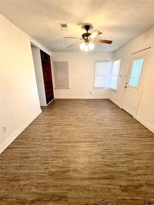 interior space featuring a textured ceiling, ceiling fan, dark wood-style flooring, visible vents, and baseboards