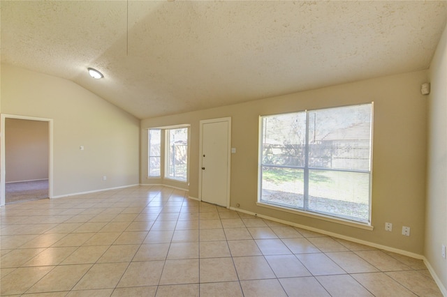 empty room with light tile patterned floors, vaulted ceiling, a textured ceiling, and a wealth of natural light