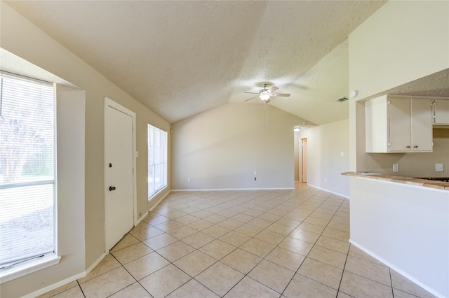 interior space with light tile patterned floors, vaulted ceiling, a textured ceiling, and a ceiling fan