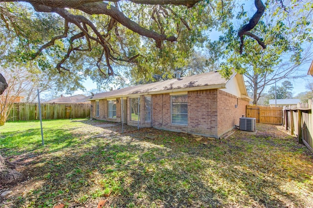 back of property featuring brick siding, a lawn, a fenced backyard, and central AC unit