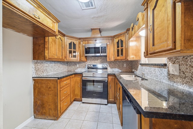 kitchen with brown cabinets, appliances with stainless steel finishes, glass insert cabinets, and a sink