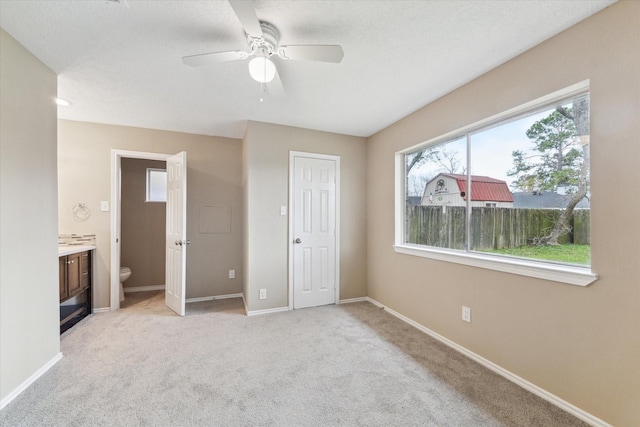 unfurnished bedroom with baseboards, light carpet, ceiling fan, and ensuite bathroom