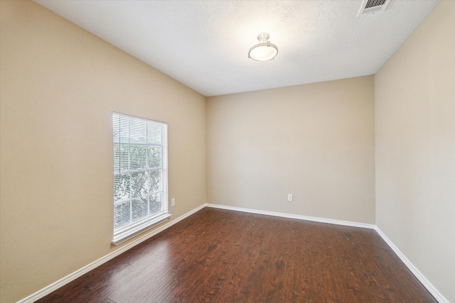 empty room featuring visible vents, dark wood-type flooring, and baseboards