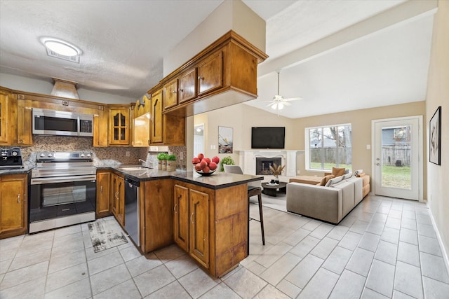 kitchen with vaulted ceiling with beams, a fireplace, brown cabinets, and stainless steel appliances