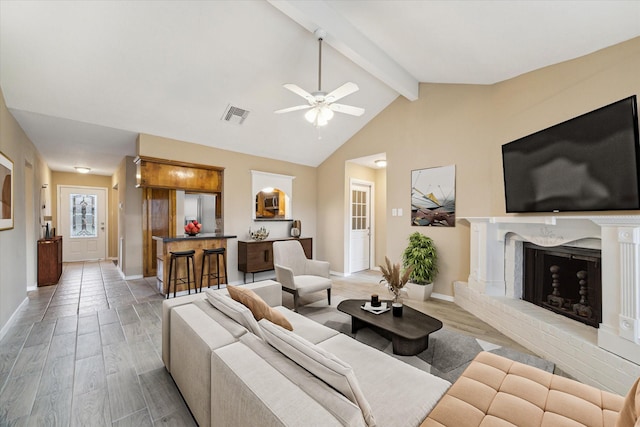 living area featuring visible vents, light wood-style floors, a brick fireplace, and vaulted ceiling with beams