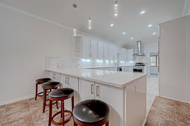 kitchen featuring stainless steel stove, backsplash, white cabinetry, wall chimney range hood, and a peninsula