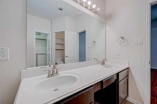 bathroom with visible vents, a sink, toilet, and double vanity