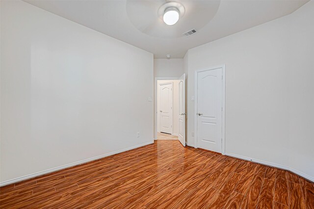 spare room with a ceiling fan, wood finished floors, visible vents, and baseboards