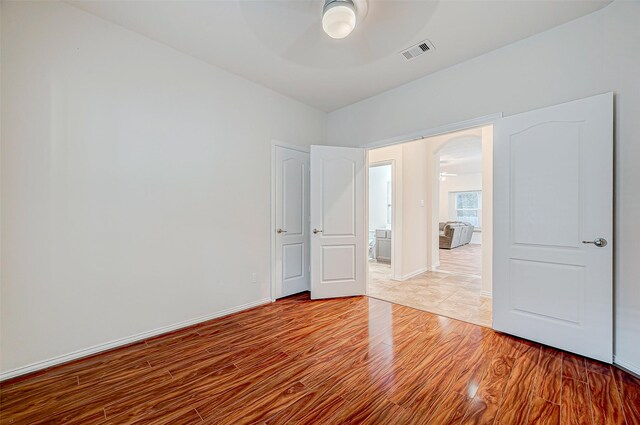 spare room featuring ceiling fan, arched walkways, wood finished floors, and visible vents