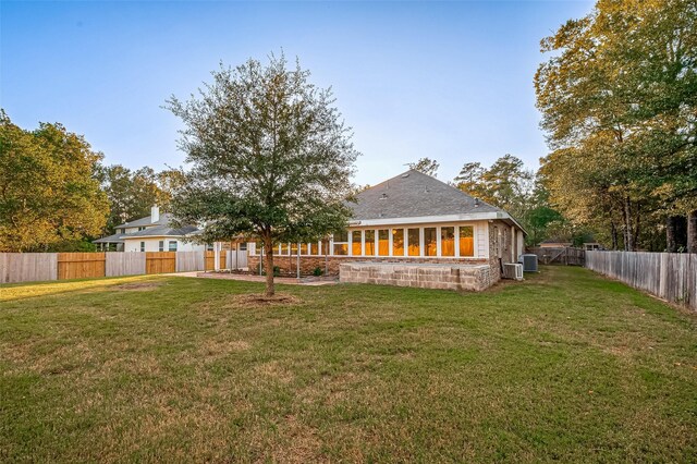 rear view of property featuring central AC unit, a lawn, and a fenced backyard