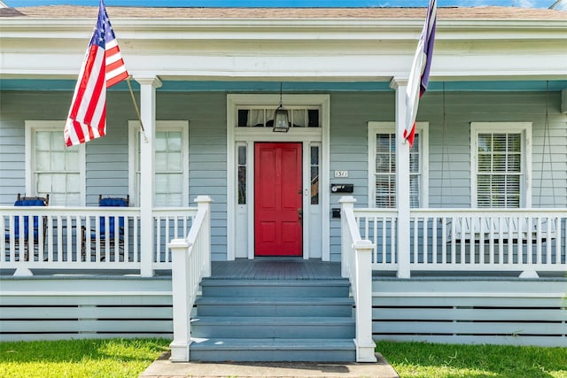 doorway to property with covered porch and a shingled roof