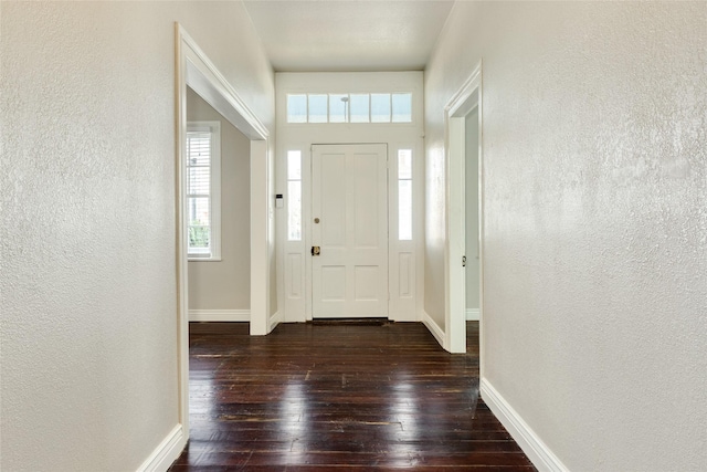 foyer entrance with a textured wall, dark wood-style flooring, and baseboards