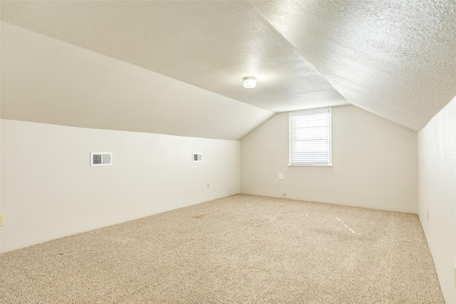 additional living space with carpet floors, lofted ceiling, visible vents, and a textured ceiling