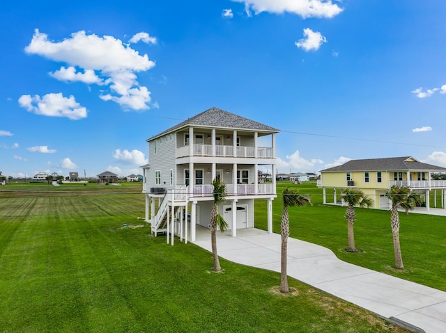 raised beach house featuring a shingled roof, a front yard, a balcony, a garage, and driveway