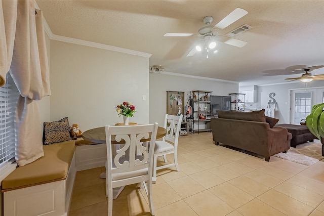 dining room with light tile patterned floors, visible vents, ornamental molding, a ceiling fan, and a textured ceiling