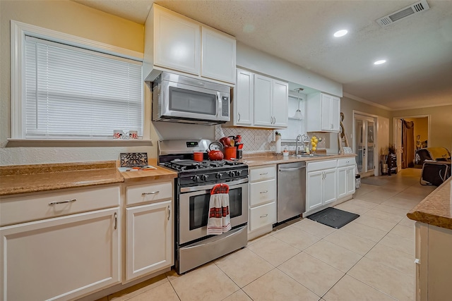 kitchen with light tile patterned flooring, stainless steel appliances, a sink, visible vents, and backsplash