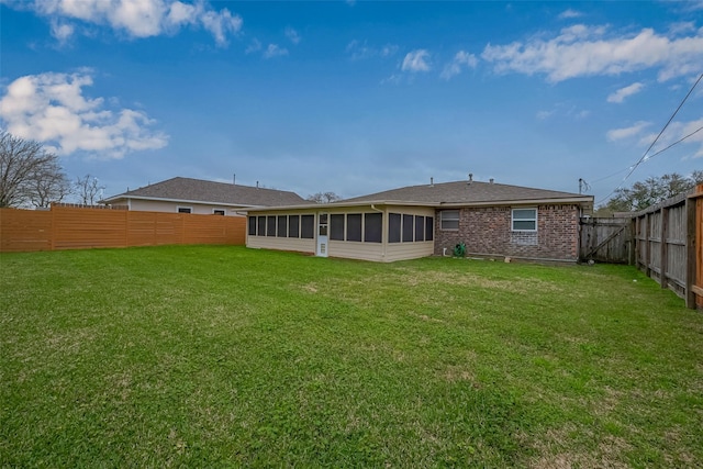 rear view of property featuring a sunroom, a fenced backyard, brick siding, and a yard