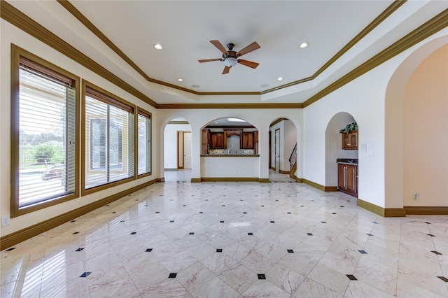 unfurnished living room featuring crown molding, a tray ceiling, arched walkways, and baseboards