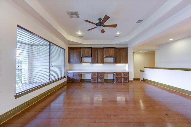 interior space with visible vents, dark wood-type flooring, a tray ceiling, and built in study area