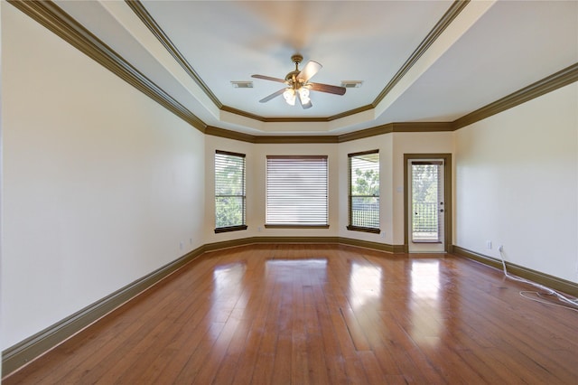 spare room with a tray ceiling, plenty of natural light, wood-type flooring, and visible vents