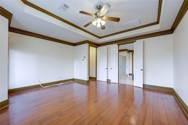 unfurnished room featuring ornamental molding, a tray ceiling, hardwood / wood-style floors, and visible vents