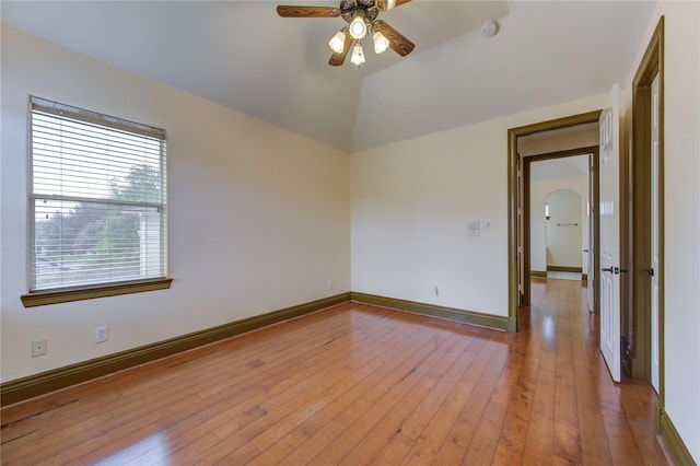 empty room featuring arched walkways, light wood-style flooring, a ceiling fan, vaulted ceiling, and baseboards