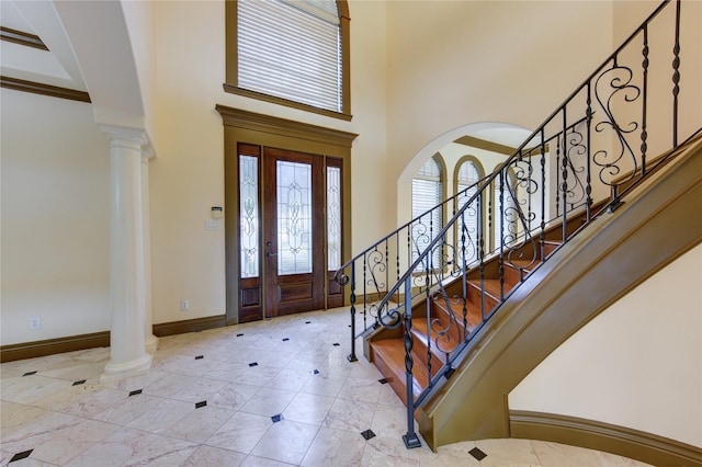 foyer featuring baseboards, decorative columns, stairway, and a high ceiling