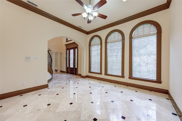 empty room featuring arched walkways, visible vents, crown molding, and baseboards