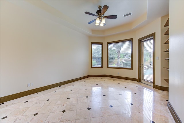 empty room with a tray ceiling, a ceiling fan, visible vents, and baseboards