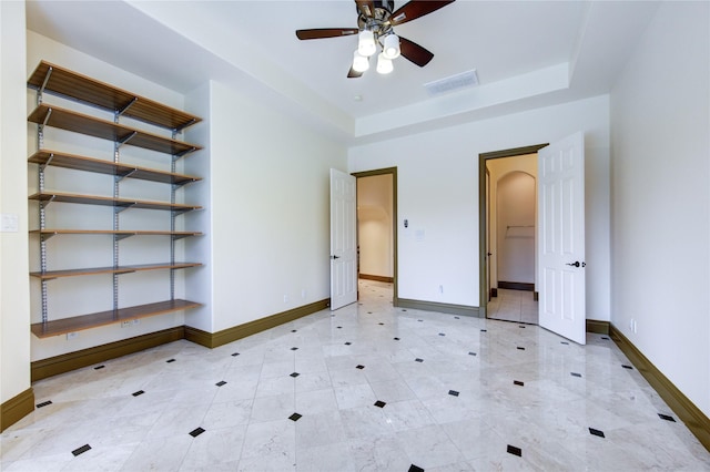 unfurnished bedroom featuring baseboards, visible vents, arched walkways, and a tray ceiling