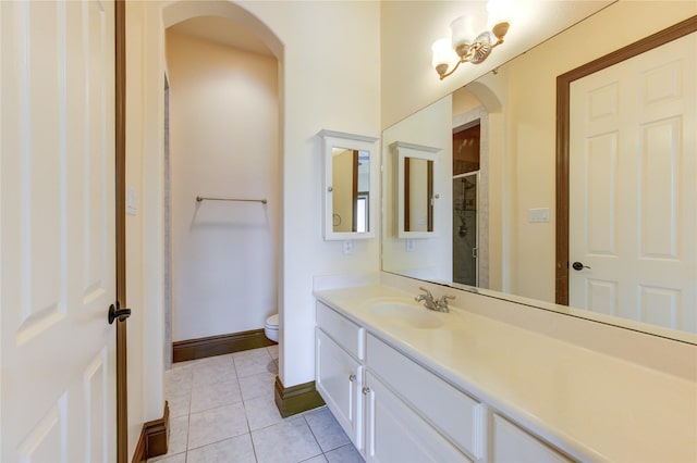 bathroom with a shower with shower door, toilet, vanity, baseboards, and tile patterned floors