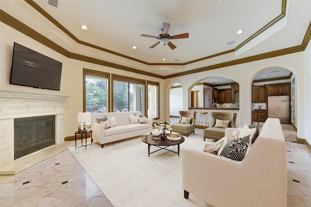 living area with baseboards, a tray ceiling, a fireplace, and crown molding