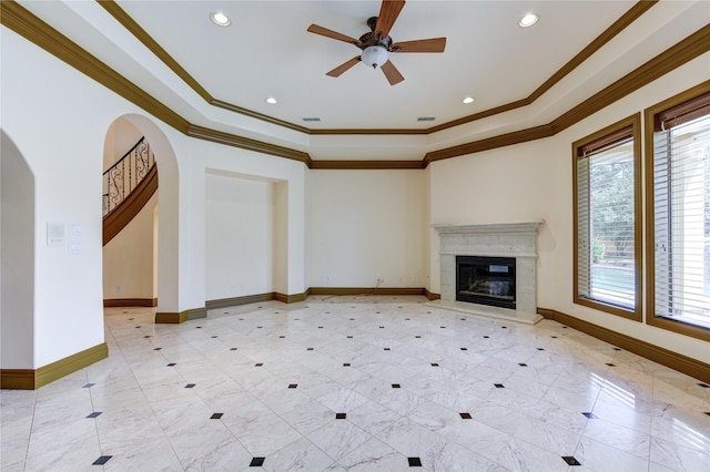 unfurnished living room featuring arched walkways, a raised ceiling, crown molding, and baseboards