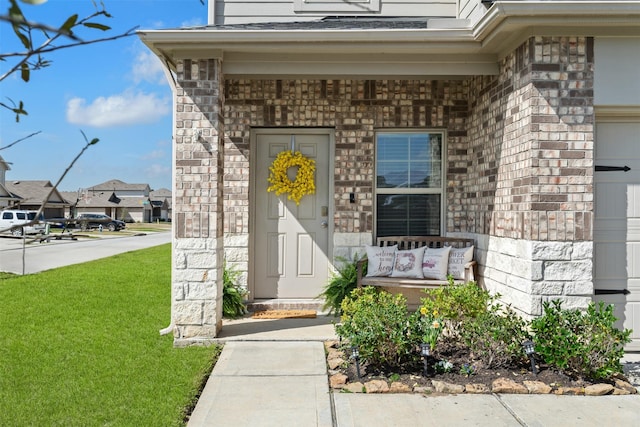 entrance to property featuring a garage, a yard, brick siding, and stone siding