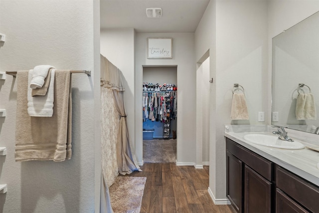 bathroom featuring a walk in closet, vanity, baseboards, and wood finished floors