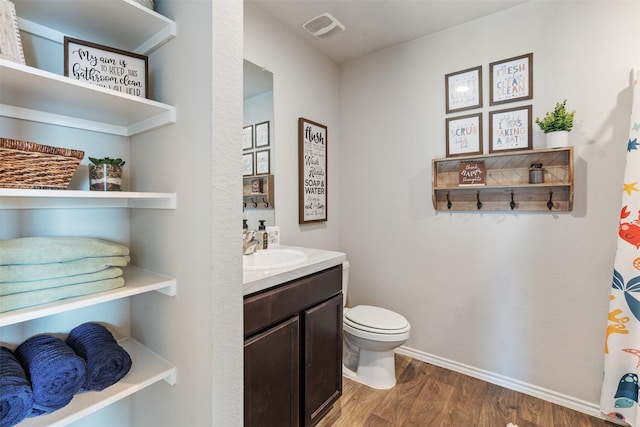 bathroom with visible vents, toilet, vanity, wood finished floors, and baseboards