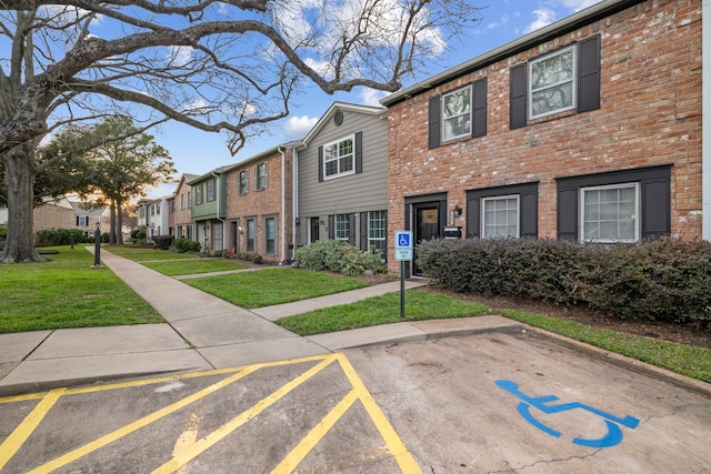 view of front of property with uncovered parking, a front yard, brick siding, and a residential view