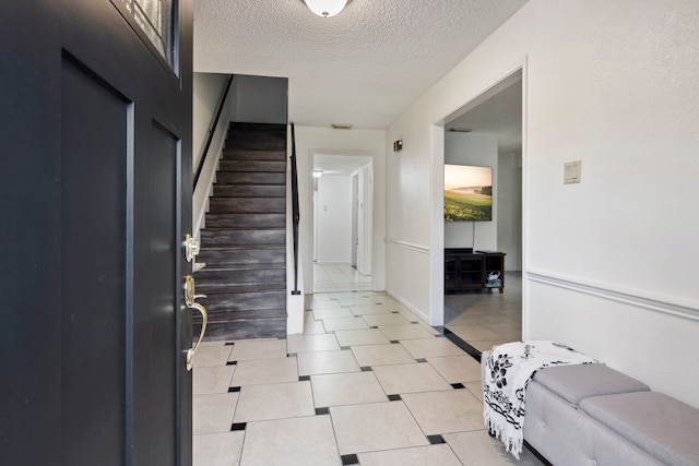 foyer entrance with light tile patterned floors, a textured ceiling, and stairs