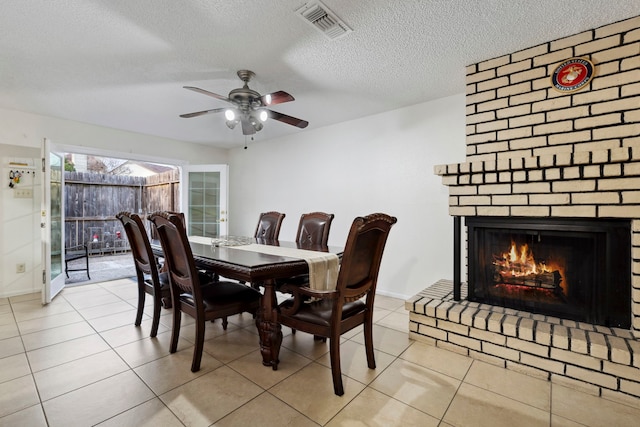 dining room featuring light tile patterned floors, ceiling fan, a textured ceiling, visible vents, and a brick fireplace