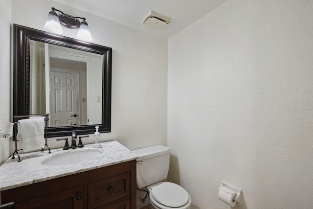 half bathroom with toilet, a textured wall, and vanity