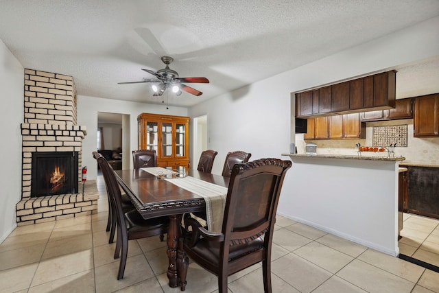 dining space with a textured ceiling, light tile patterned floors, a fireplace, and a ceiling fan