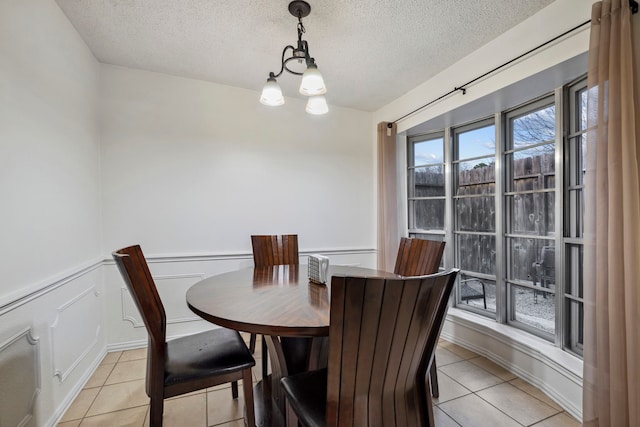 dining space featuring light tile patterned floors, a wainscoted wall, a textured ceiling, and a decorative wall