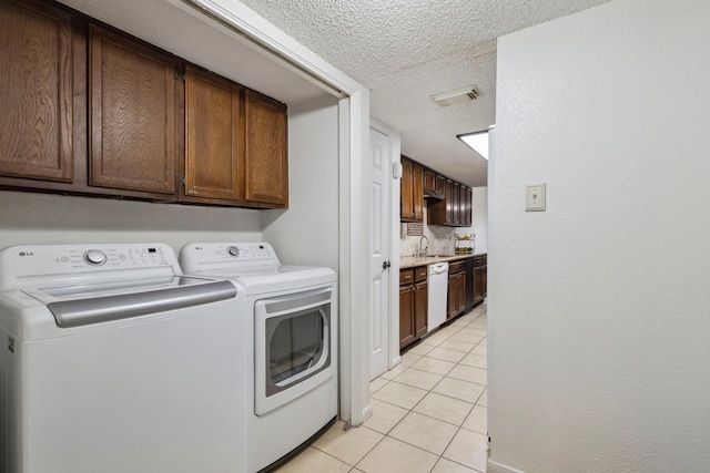 laundry area with a textured ceiling, light tile patterned flooring, visible vents, washer and dryer, and cabinet space