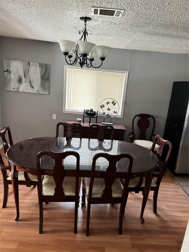 dining space featuring a textured ceiling, a textured wall, light wood-style flooring, visible vents, and an inviting chandelier