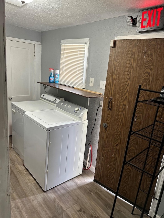 washroom with light wood-style floors, washing machine and dryer, a textured ceiling, and a textured wall