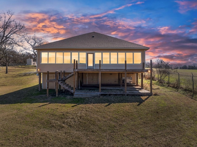 back of property at dusk featuring a shingled roof, a lawn, a sunroom, stairway, and fence
