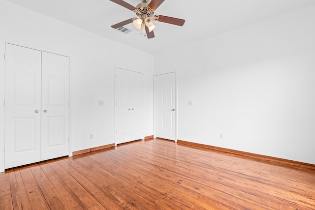 unfurnished bedroom with two closets, visible vents, light wood-style floors, a ceiling fan, and baseboards