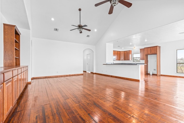 unfurnished living room with arched walkways, high vaulted ceiling, visible vents, baseboards, and hardwood / wood-style floors